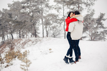 Wall Mural - Young couple in a winter park. Man with a red sharf. Lady in a red jacket