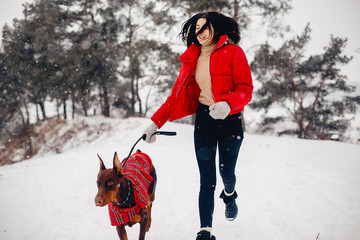 Wall Mural - Cute girl walking in a winter park. Woman in a red jacket. Lady with a dog