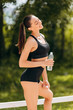 © speed300 - Happy sporty woman standing in the park holding a bottle with water outdoor. - Image