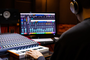 back of asian male music producer arranging a song on midi keyboard and computer in home recording studio. music production concept