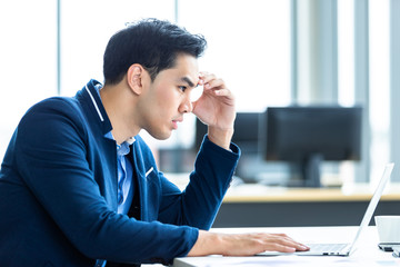 Stressed businessman worked with laptop computer and having a headache after business losses In the office room background.