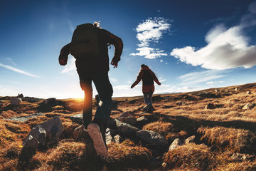 Couple hikers run and jump against sunset mountains