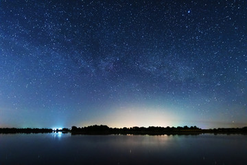 Wall Mural - a magical starry night on the river bank with a large tree and a milky way in the sky and falling st