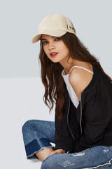 Wall Mural - Full length shot of a dark-haired girl, sitting on a floor and wearing beige baseball cap with lettering 