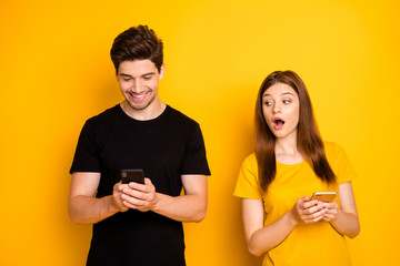 Poster - Photo of couple with her looking into her guy screen and him chatting to his lover wearing black t-shirt smiling toothily isolated over bright shiny color yellow backgound