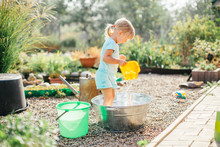 Little Blonde Girl Playing At Garden With Water In A Tin Basin. Kids Gardening. Summer Outdoor Water Fun. Childhood In The Country