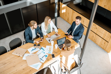 Business people working with computers and some printed statistics at the wooden table in the meeting room, view from the above