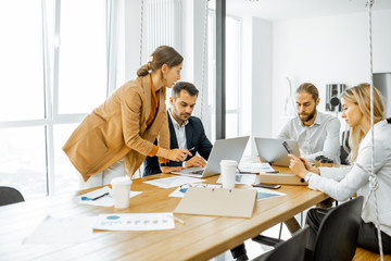 Group of a young office employees dressed casually in the suits having some office work at the meeting table in the bright office