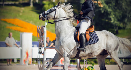 The girl rider sits in the saddle on a fast galloping gray horse and which performs at competitions on show jumping