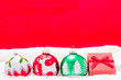 canvas print picture - Drei Christbaumkugeln und eine Rote Geschenkbox im Schnee vor einem Roten Hintergrund
