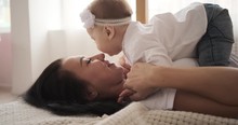 Mother Kissing Adorable Baby Daughter Lying On Her Stomach In Bed