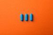 Blue capsules pills on orange background, closeup and space for text