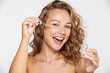 Image of excited half-naked woman smiling and using facial serum