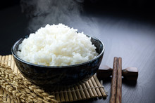 Cooked Jasmine Rice In Ceramic Cups And Chopsticks And Ear Of Rice Placed On A Black Wooden Table. Close Up Shot. 45 Degree Angle.