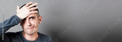 Fotomural confused young man holding his head, having regret, grey banner