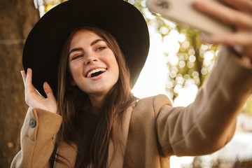 Sticker - Portrait of smiling woman taking selfie photo while walking in autumn park