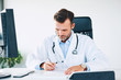 © baranq - Doctor sitting in office and taking care of paperwork between patient visits