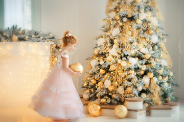 Wall Mural - 5 years old girl in beautiful light pink dress with creamy golden ball in christmas time near christmas tree