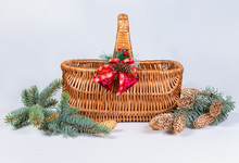 Empty Wicker Basket With Red Ribbon And Toys, Next To Fir Branches With Cones Isolated