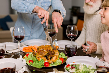 Wall Mural - Cropped image of the hands of young father carving Thanksgiving turkey for his family sitting at the table