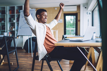 Excited man celebrating success at desk with laptop