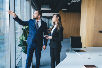 Wall Mural - Focused colleagues having conversation and pointing at window while standing at office