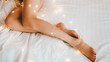 Festive mood. Cropped shot of woman with beautiful legs and smooth skin lying down on bed with sparkling fairy lights.