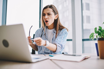 Wall Mural - emotional woman stressed while watching video on laptop computer sitting in office interior, shocked