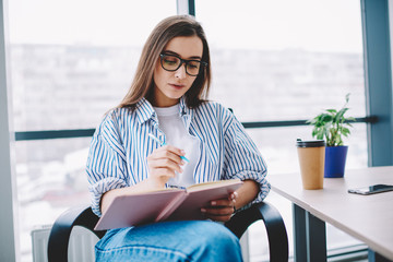 Wall Mural - clever female employee in eyewear writing in notepad concentrated on working process in office, seri