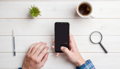 Wall Mural - man hold smart phone with blank screen for mockup. top views, flat lay composition with white wooden