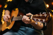 © dikushin - Guy plays guitar close-up. Against the background of a decorated Christmas tree with a garland