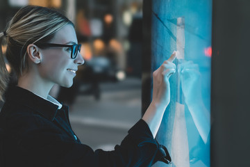 Wall Mural - smiling female standing at big display with advanced digital technology. young woman touching with f