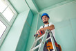 © Studio Romantic - A builder standing on a ladder installs drywall at a construction site