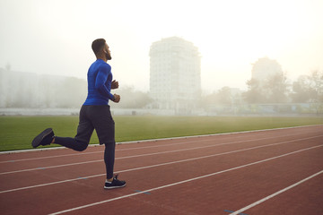 Wall Mural - A young athlete runs on a stadium in the fog.