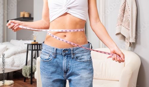 Fotomural Slim woman standing in front of the mirror measuring her waist after weight loss