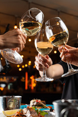 People clink glasses with white wine above a table full of meals in a restaurant