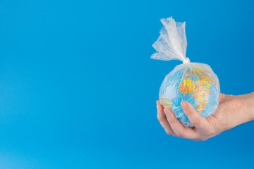 hand holding planet earth inside a plastic bag over blue background with room for text.