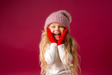 Little Blonde Girl In A Knitted Hat And Mittens Smiles. Winter Clothes