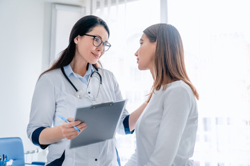 Doctor talking to female patient in working cabinet at hospital