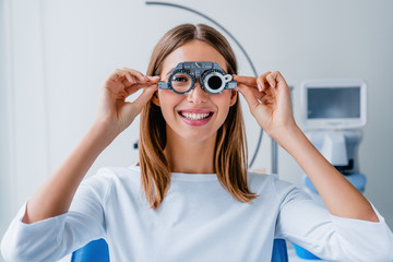 Wall Mural - Young woman checking vision with eye test glasses during a medical examination at the ophthalmological office