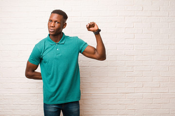 young african american black man feeling serious, strong and rebellious, raising fist up, protesting or fighting for revolution against brick wall