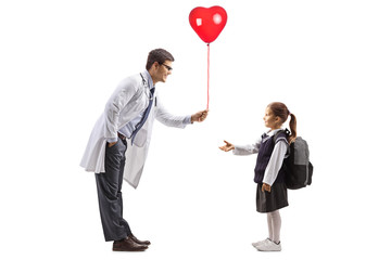 Wall Mural - Male doctor giving a heart shaped balloon to a schoolgirl