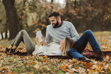 Wall Mural - Young happy couple reading book together in autumn