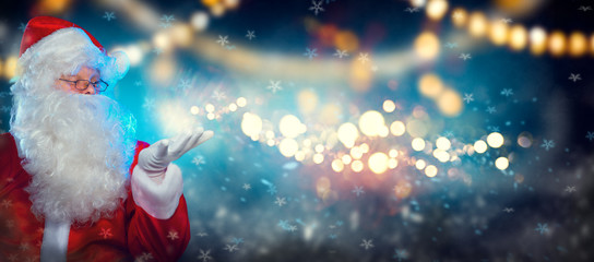 Santa Claus with magic gift in his hands. Portrait of happy Santa Claus making magic at night, Blowing Magic Christmas Stars, pointing hand over holiday night background