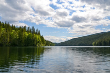 The Dense Pine Forest Lining The Edges Of Clearwater Lake Reflects On The Rippled Water. The Clouds And Trees Reflect On The Surface Of The Lake On This Calm And Sunny Day.