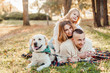 © zadorozhna - Happy family is having fun with dog labrador are lying on green grass in park.