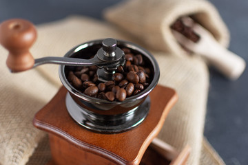 Manual vintage coffee grinder and coffee beans in a burlap bag on a wooden table.