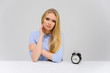 Concept cute model misses losing time sitting at the table. Close-up portrait of a beautiful blonde girl with excellent makeup with long smooth hair on a white background in a blue shirt.