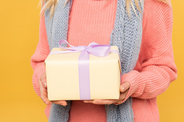 Cropped view of woman on sweater holding gift box isolated on yellow