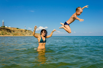 A young mother in a swimsuit plays with her young son in the sea.